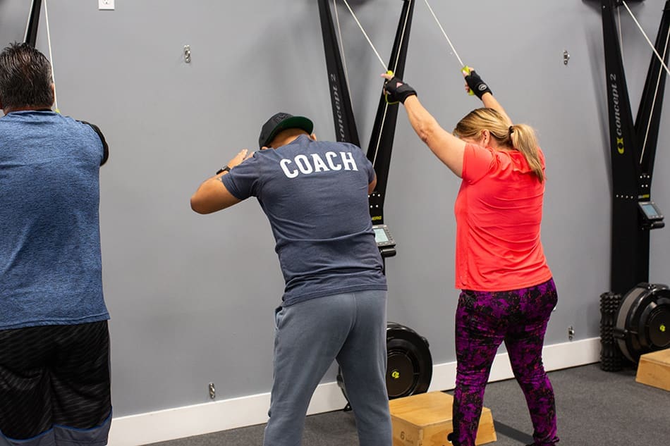 A Coastal Fitness coach helping a member with the Skiergs